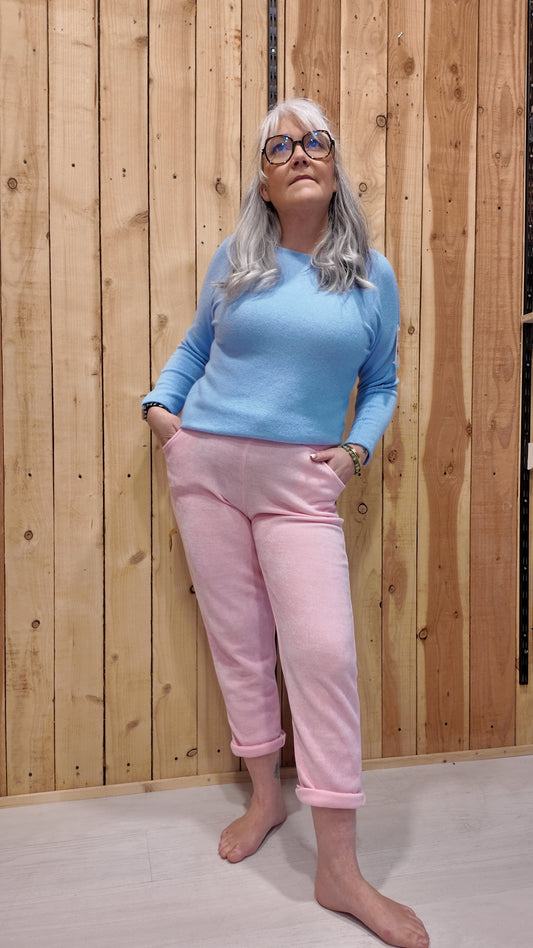 Femme portant un pantalon effet velours rose malabar coupe droite avec revers, associé à un pull bleu ciel.